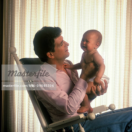 846-09085306em-1980s-father-sitting-in-rocking-chair-holding-crying-baby-fatherhood.jpg