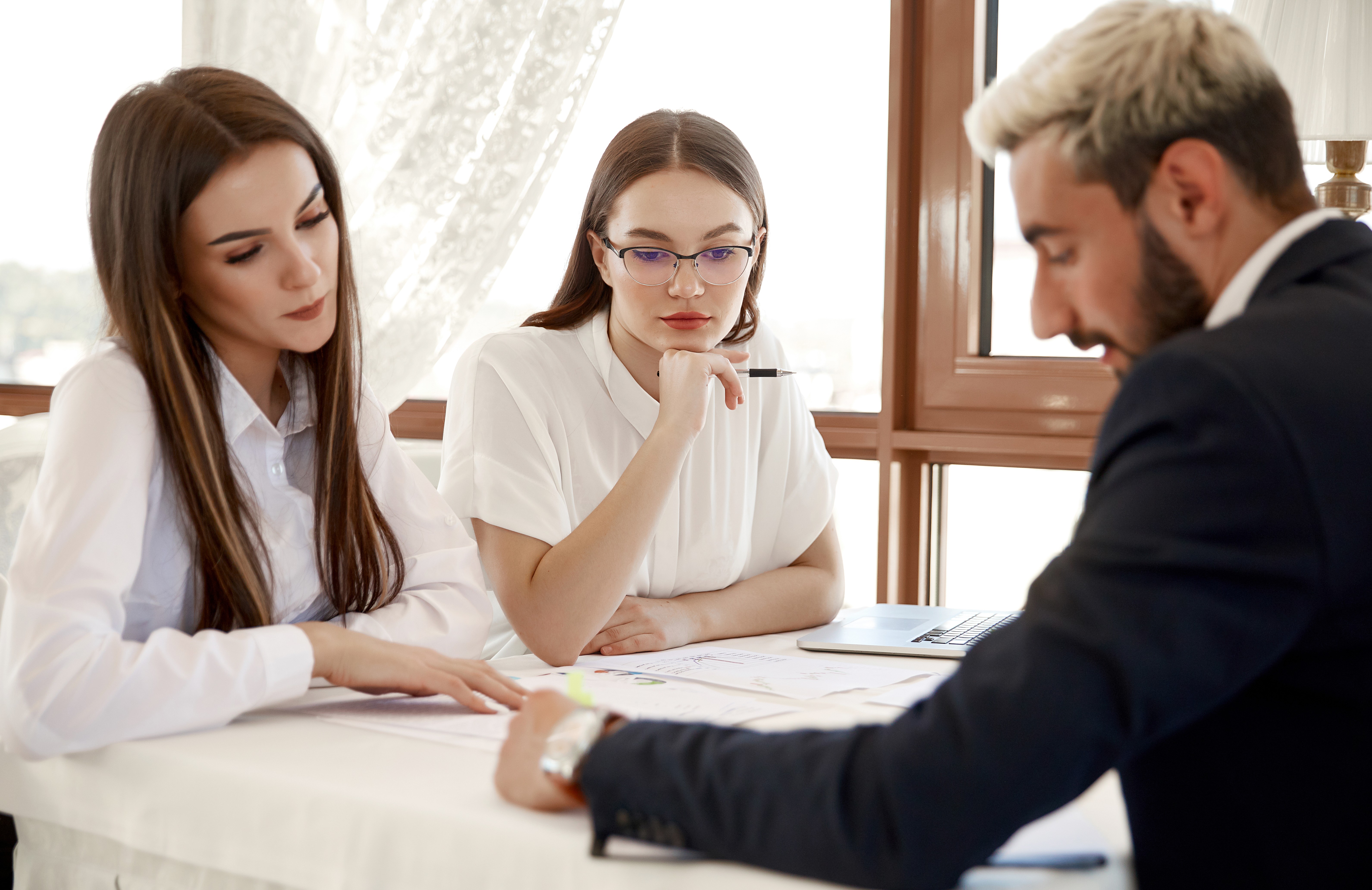 A business professional explains documents to two colleagues during a formal office meeting.