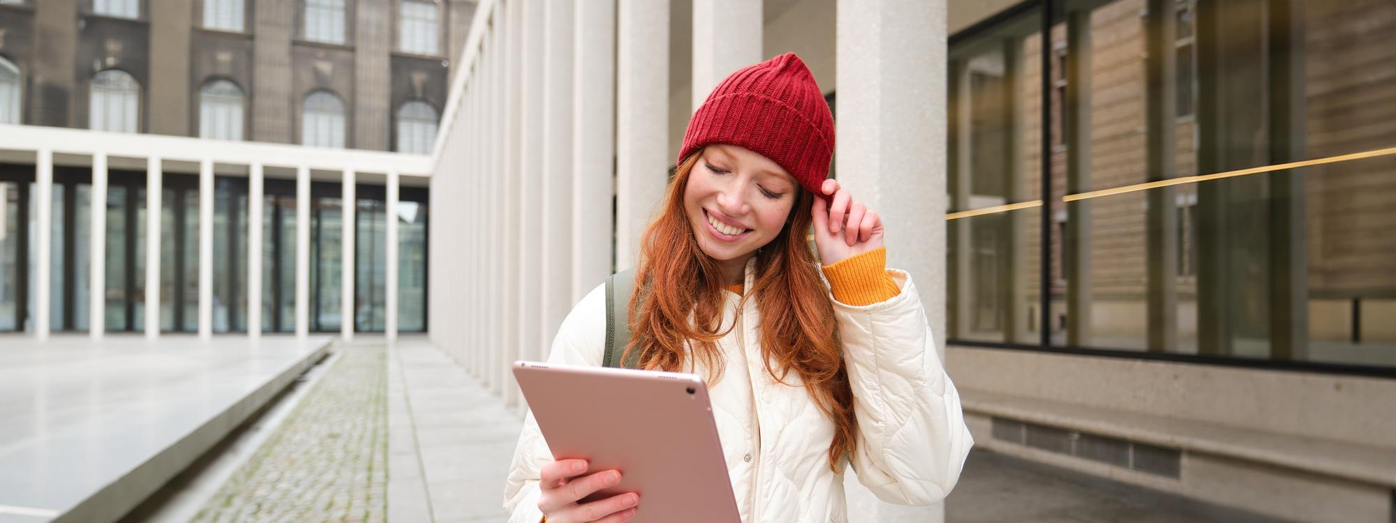 una-felice-ragazza-rossa-con-il-cappello-rosso-cammina-per-la-citta-con-un-tablet-digitale-che-si-connette-alla-rete-internet-wi-fi-pubblica.jpg