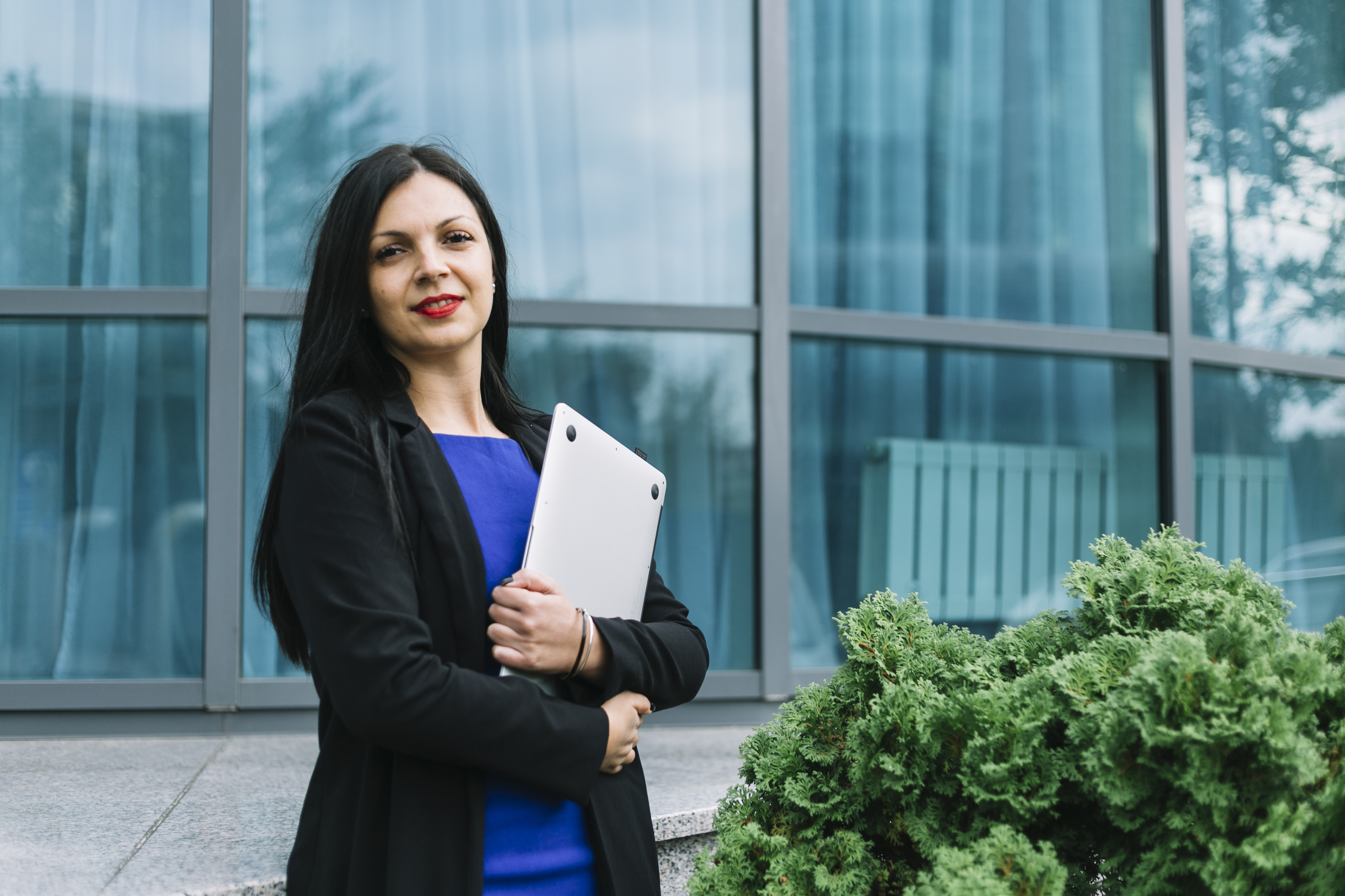 portrait-smiling-businesswoman-holding-laptop-front-glass-building.jpg