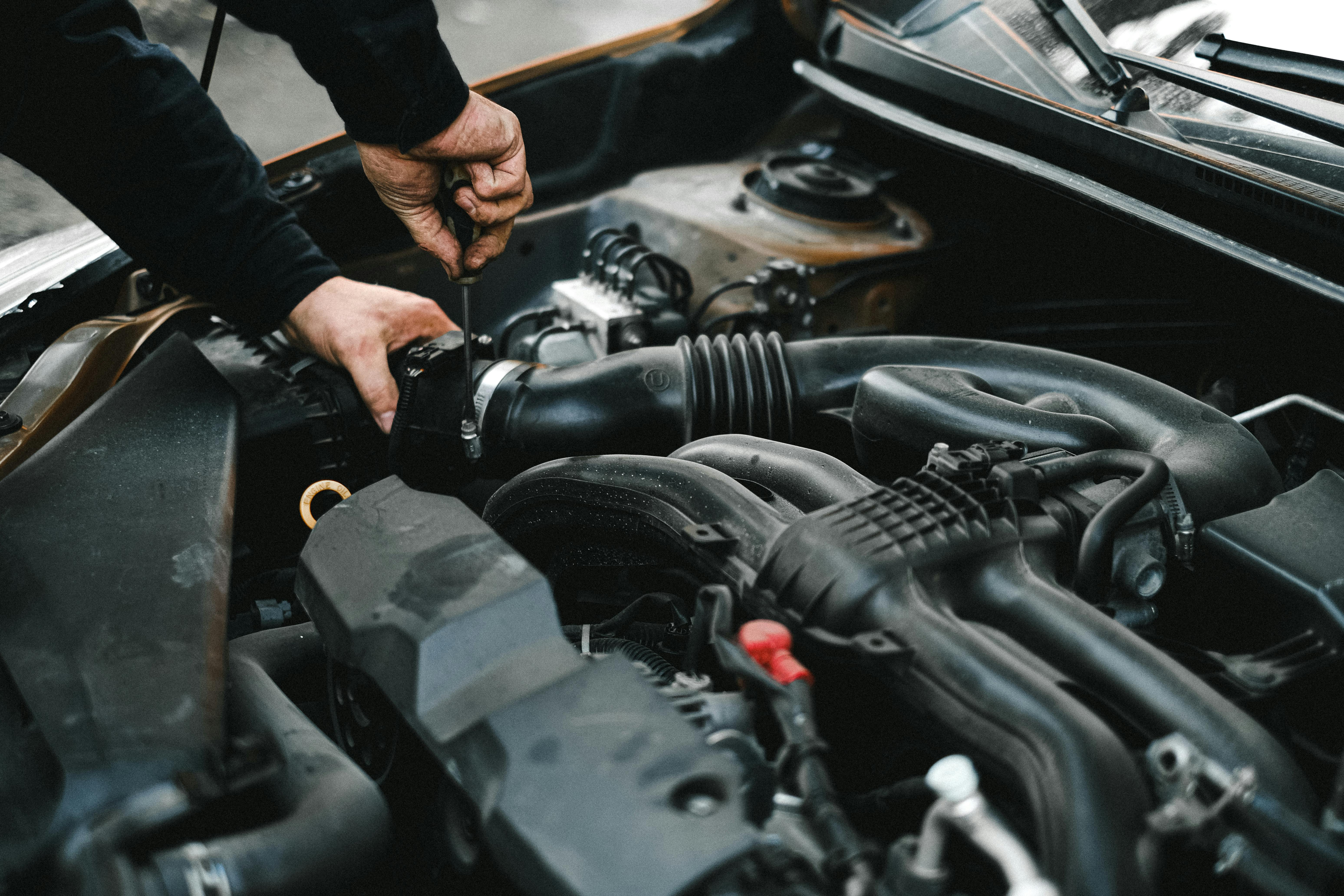 Close-up of a mechanic’s hands using a screwdriver to work on a car engine inside the open hood