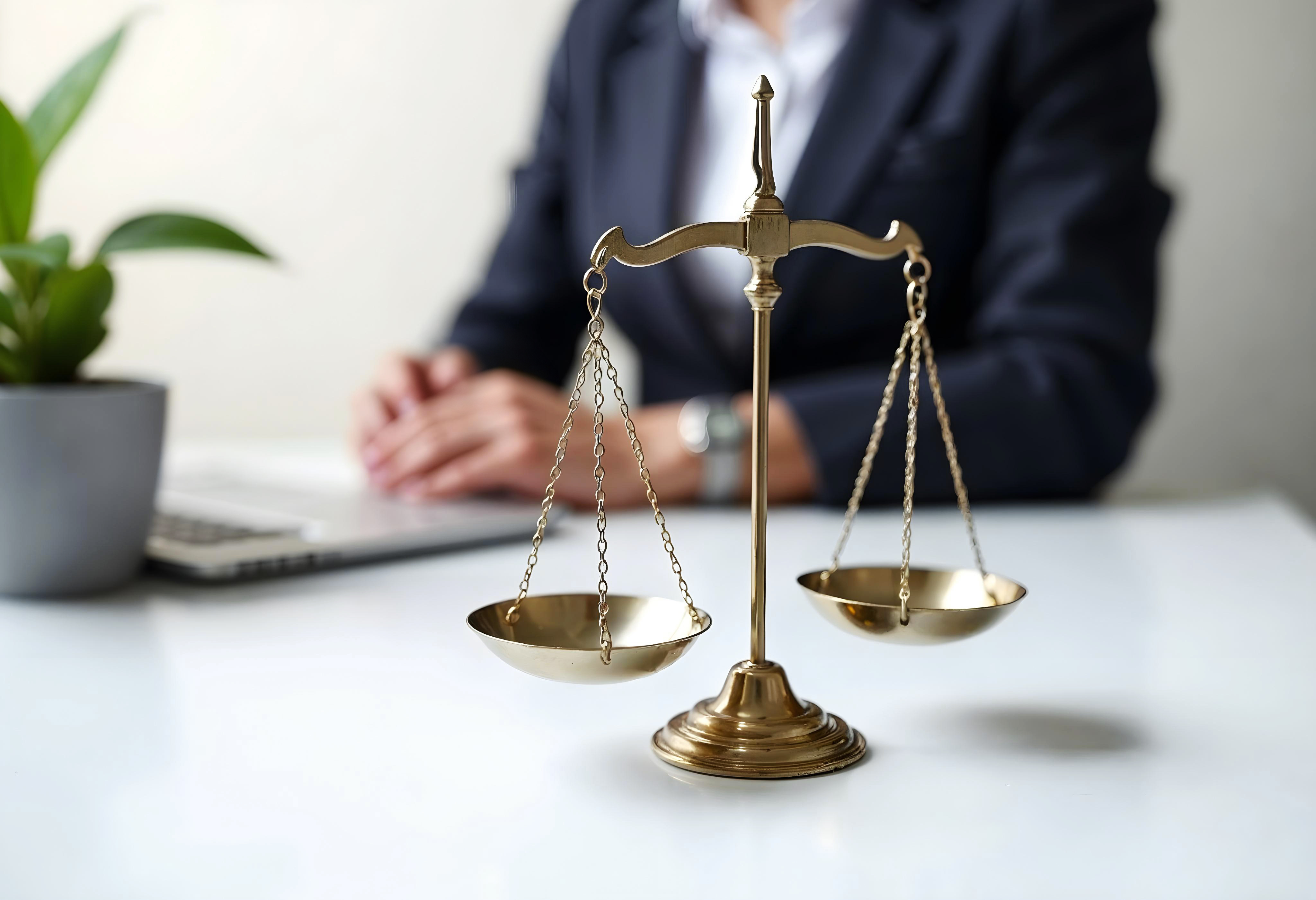 Scales of justice on a desk with a legal professional seated in the background, representing law, fairness, and legal counsel.