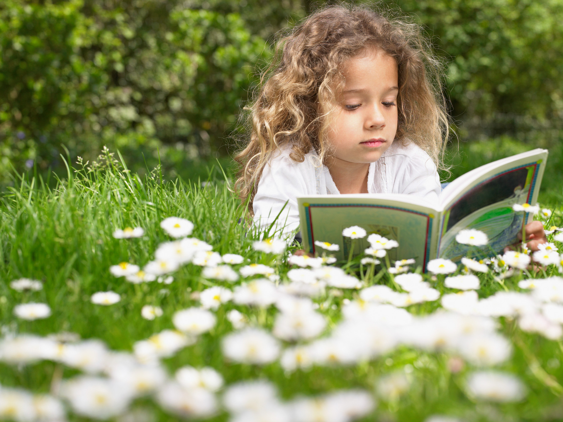 Little girl reading a book while lying on the grass.jpg