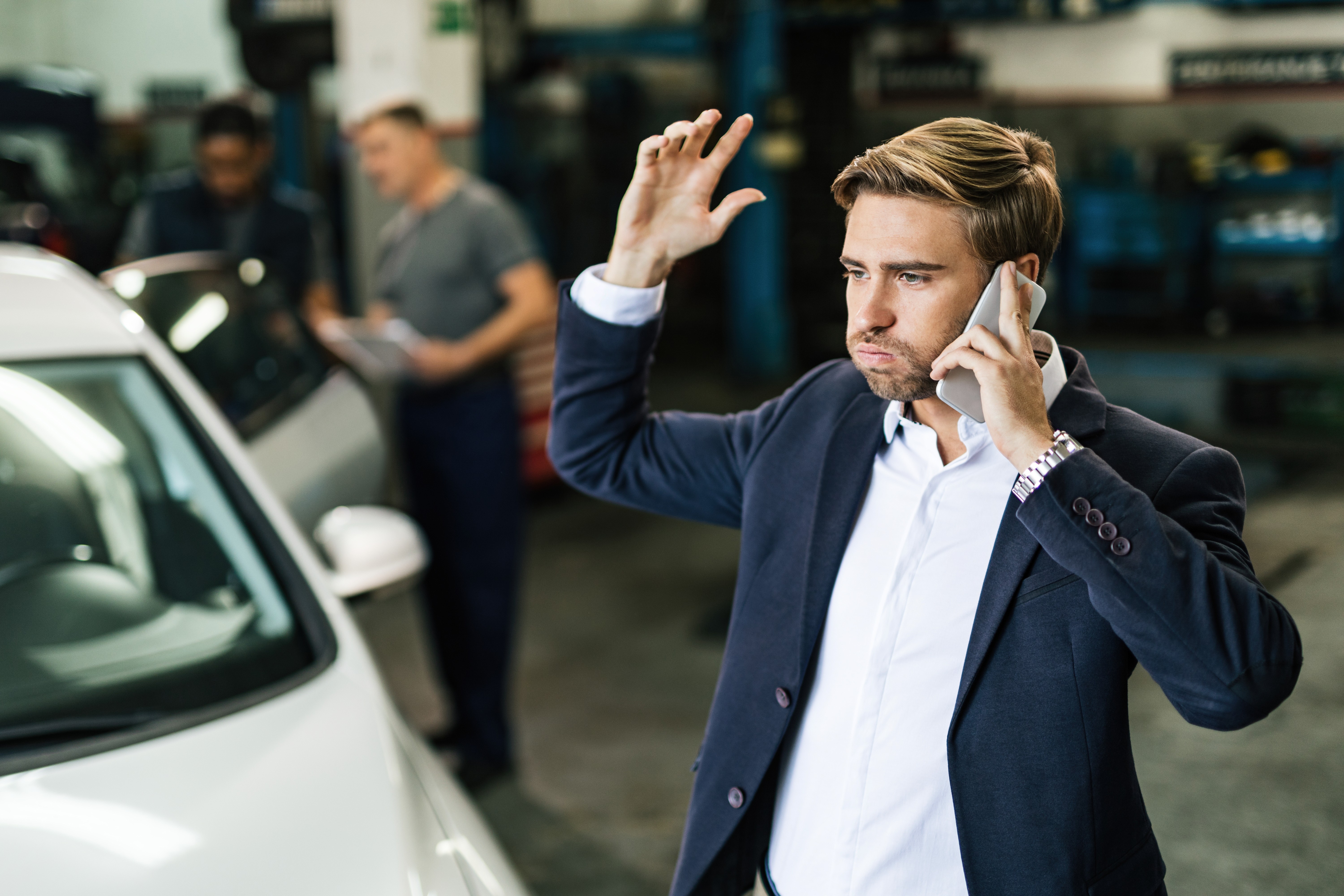 young-displeased-businessman-talking-phone-while-being-car-repair-workshop.jpg