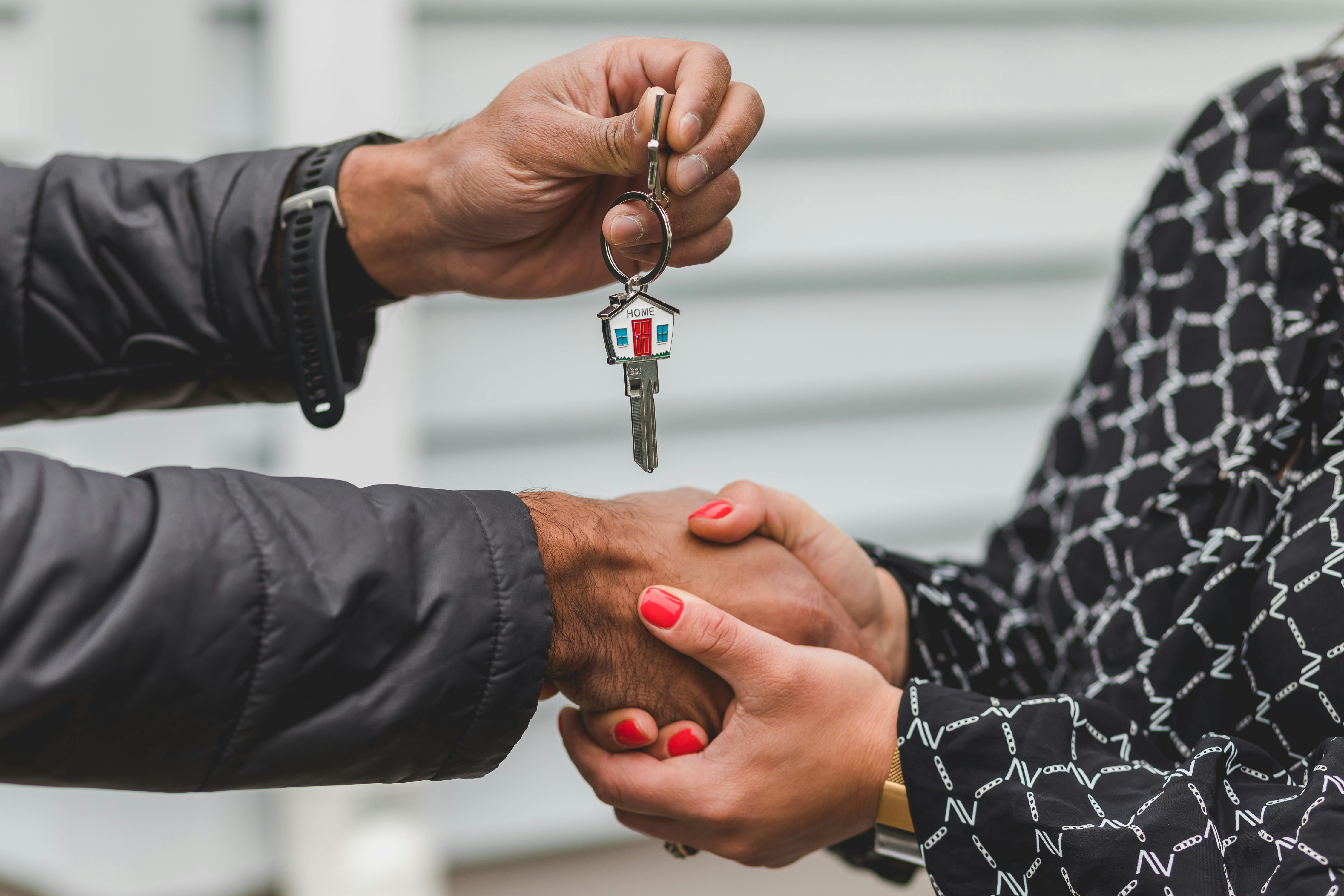 Two people shake hands as one person hands over a keyring with a house-shaped keychain.