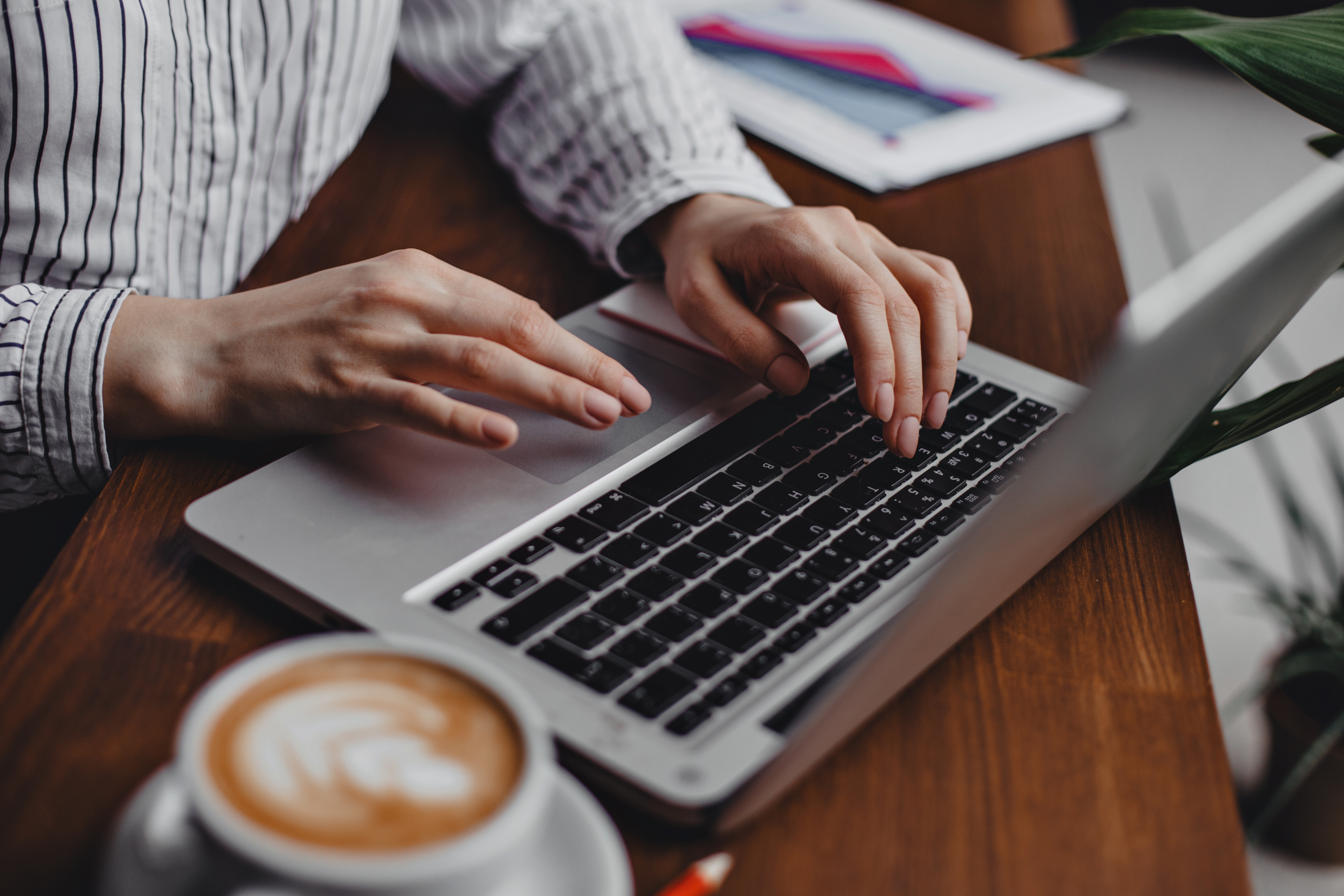 female-hands-press-laptop-keys-while-sitting-at-wooden-table-with-white-cappuccino-cup.jpg